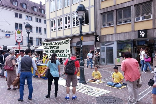 Two practitioners meditate in Freiburg. Next to them is a practitioner talking to passersby about Falun Dafa and the persecution in China.