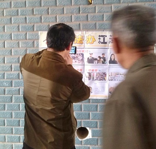 One person reads a poster in Nanchong City in Sichuan Province in central China, while another takes a picture.